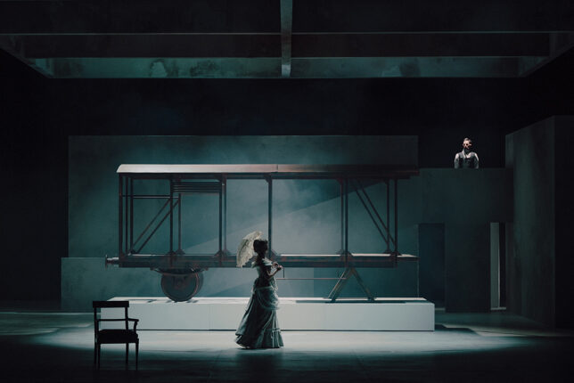 fotos ze spektaklu przedstawia damę z parasolką na tle industrialnego wozu