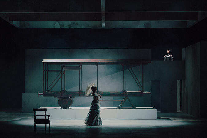 fotos ze spektaklu przedstawia damę z parasolką na tle industrialnego wozu