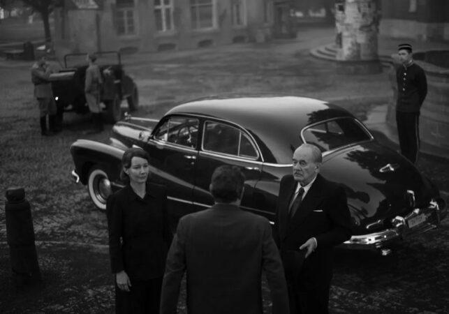czarno-biały kadr z filmu przedstawia troje osób przy starym eleganckim samochodzie